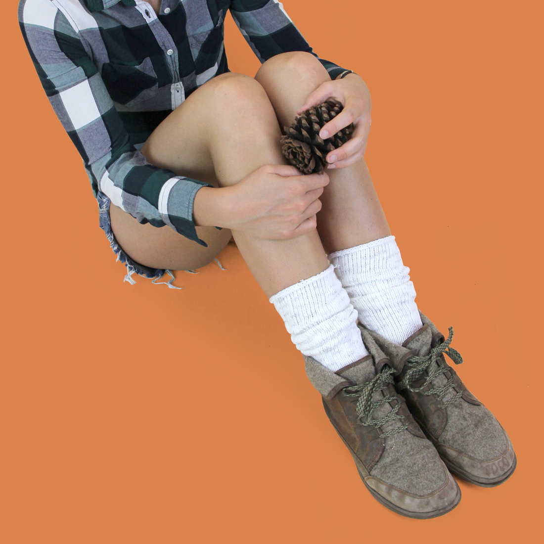 Cotton rag boot socks on a model in hiking boots, shorts, and a flannel shirt holding a pinecone.