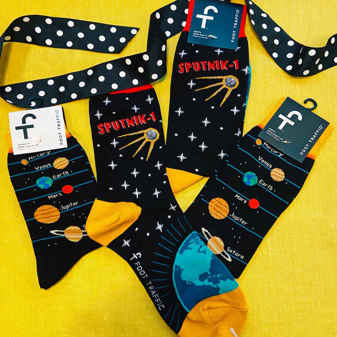 Sputnik and planets design socks on a yellow background with a black polka-dot ribbon.