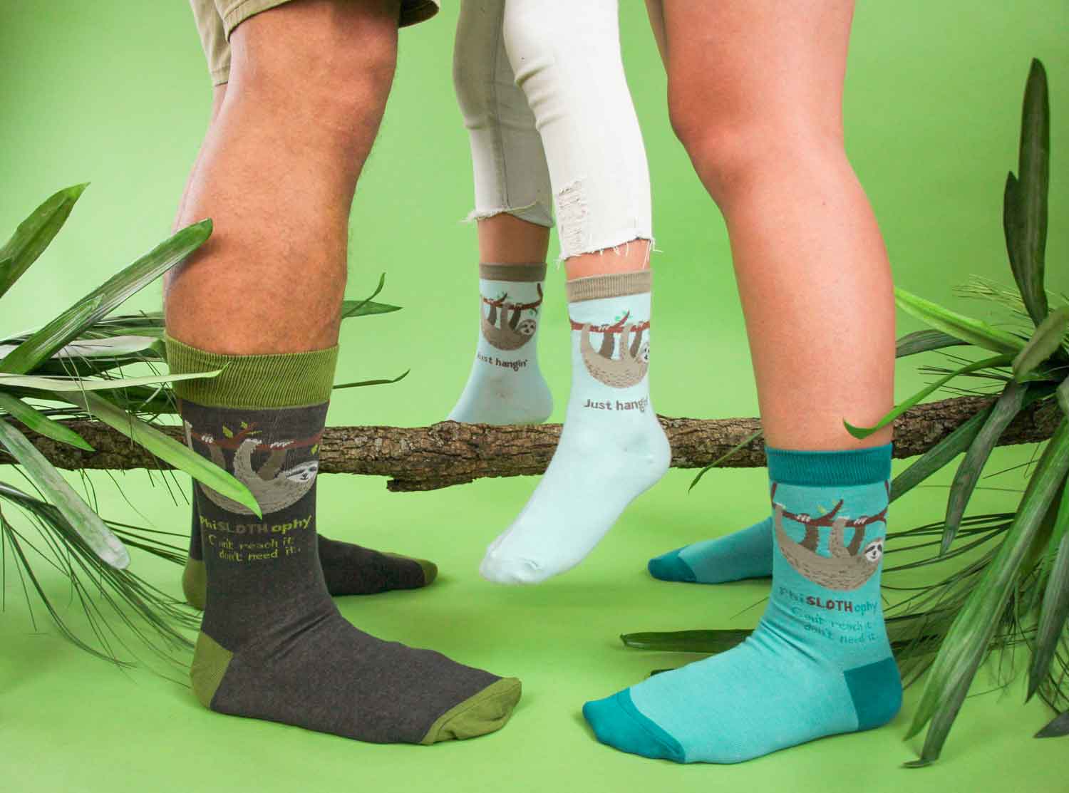 A man and woman holding up a kid in between them, all wearing Sloth design socks against a green background with foliage surrounding them.